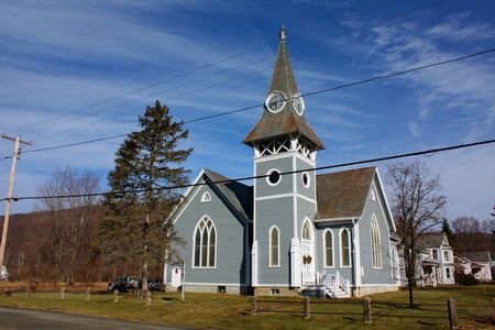 The pale blue clapboard church building with its pointed-arch windows and clock steeple, seen from the road on a clear winter day.